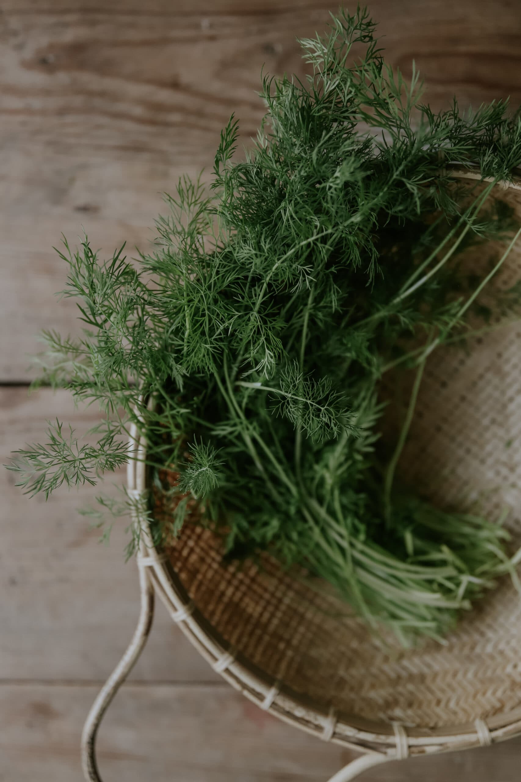 grön dill inuti korg ovanpå brunt bord