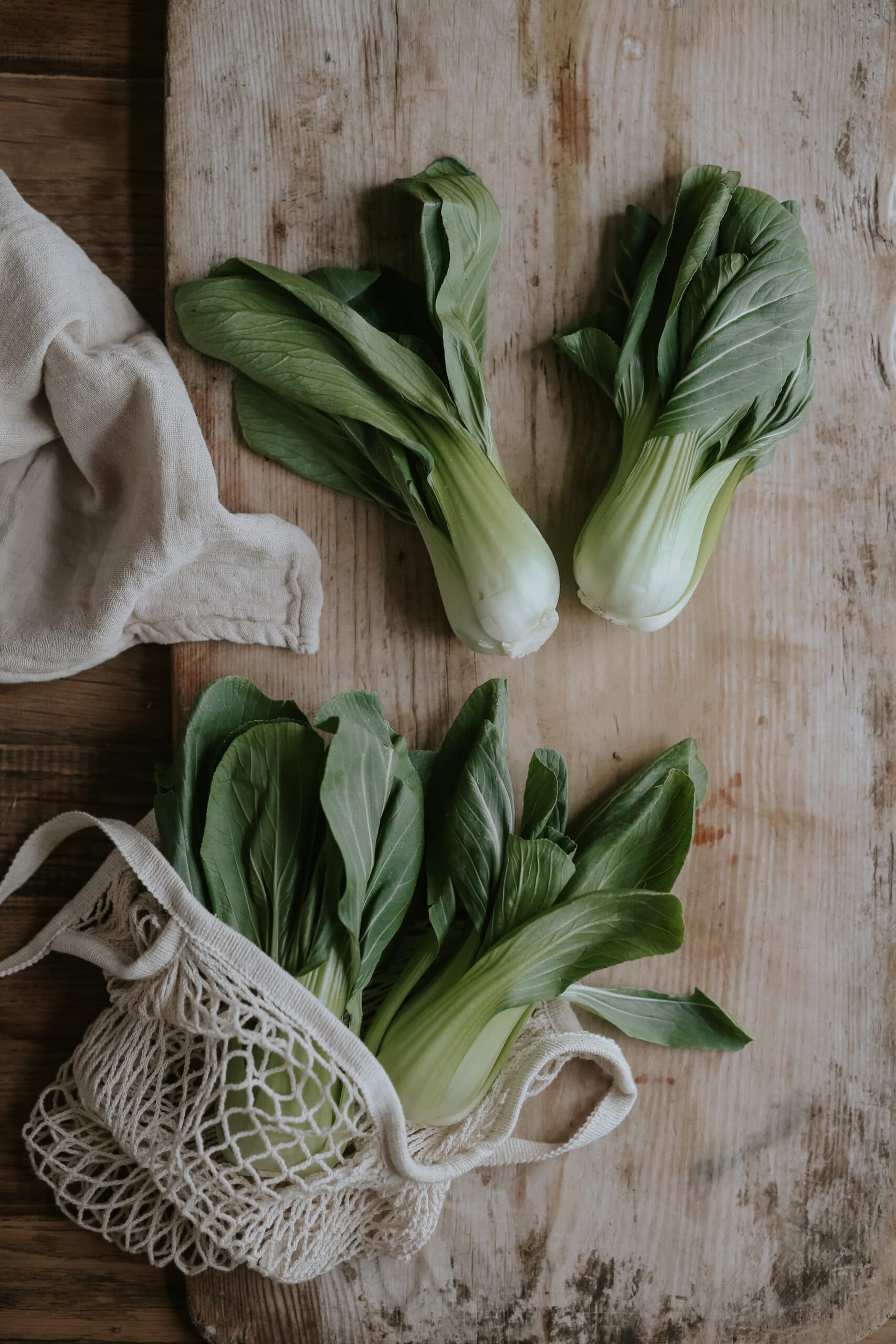 två pak choi upplagda på brunt bord bredvid påse med fler pak choi